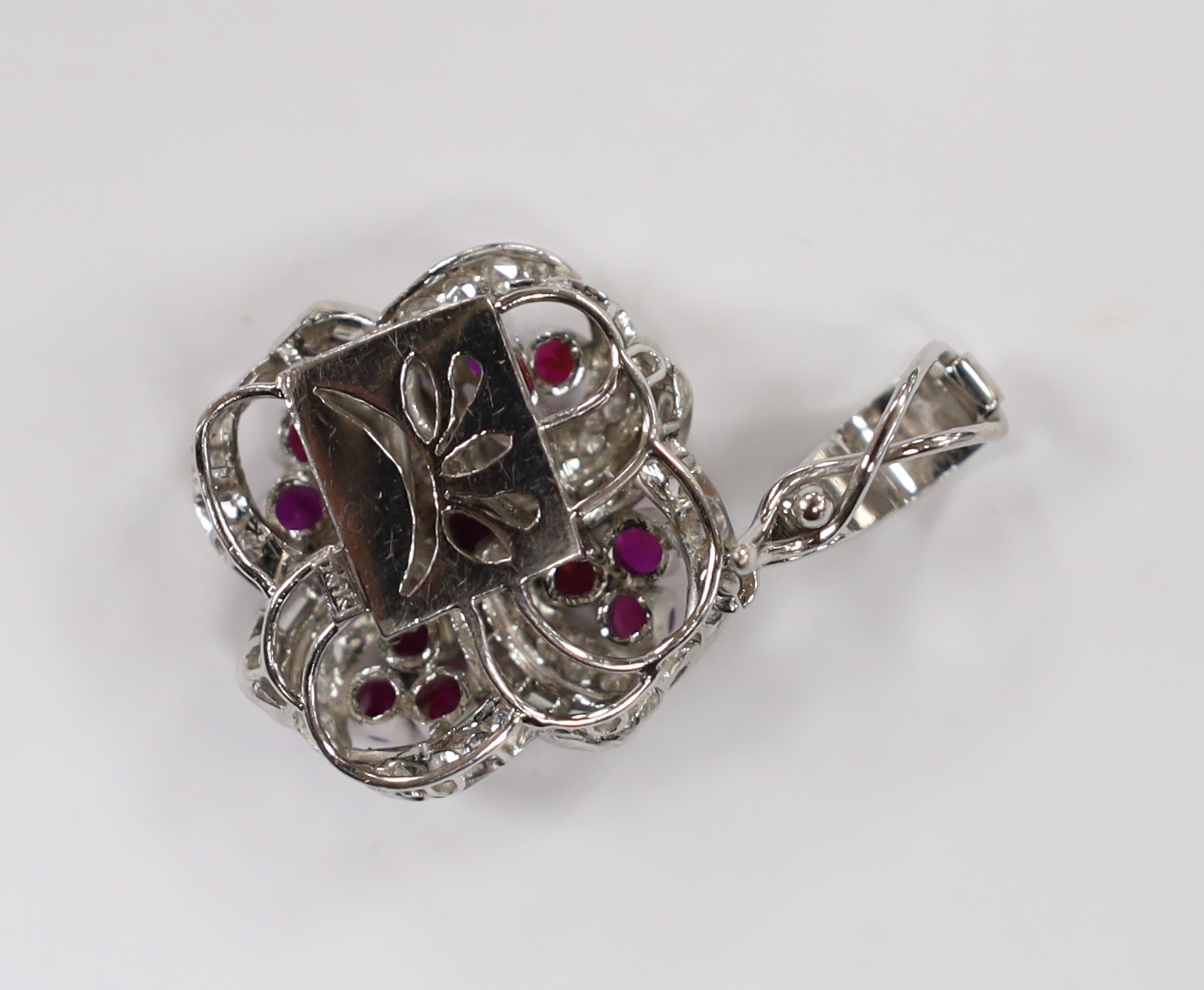 A modern 14k white metal, ruby and diamond cluster set scroll pendant, 25mm, gross weight 11 grams.